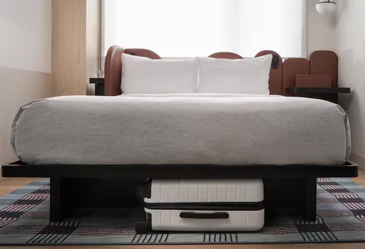 Doppelbett mit weißem Bezug und einem unter dem Bett verstauten weißen Koffer.