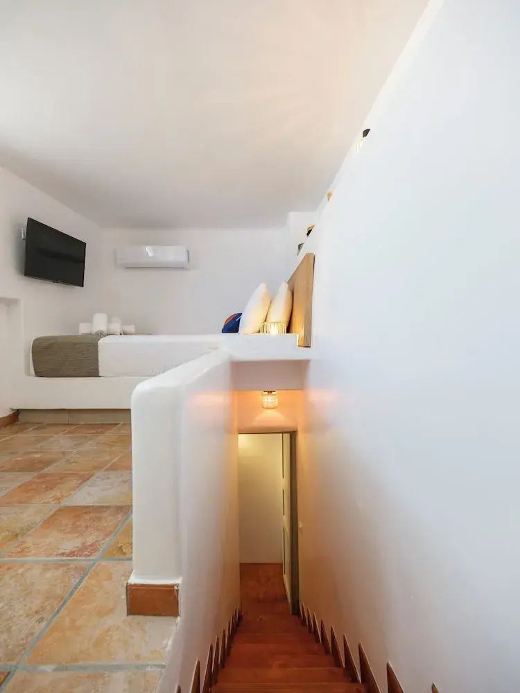 Zimmer auf zwei Ebenen mit erhöhtem Bett, weiß getünchten Wänden und kleiner Treppe.