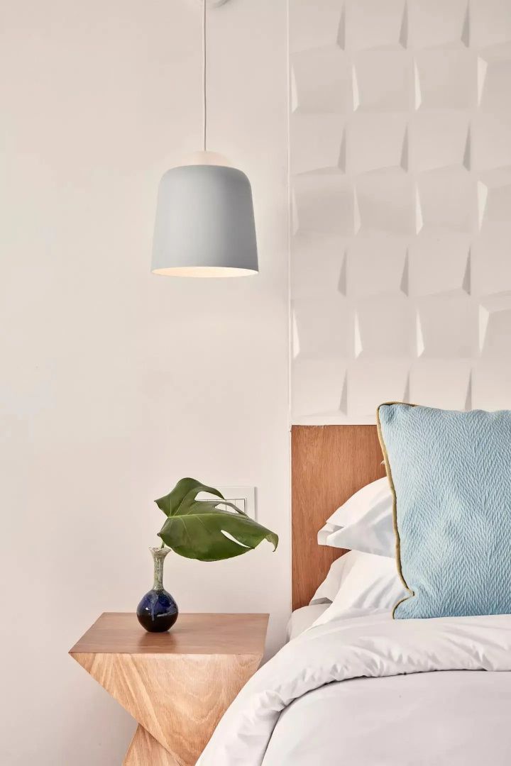 Hellblaue Lampe hängt neben einer strukturierten Wand über einem Nachttisch im Zimmer.