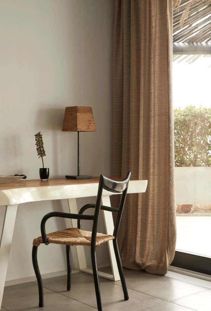 Schreibtisch aus Holz mit kleiner Tischleuchte und Stuhl mit Geflecht.