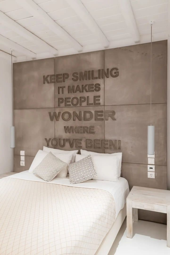 Doppelbett mit weißer Tagesdecke vor einer Wand mit englischem Schriftzug.