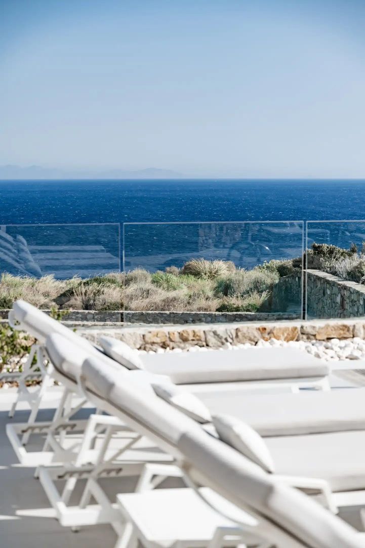 Sonnenliegen auf einer Terrasse mit Glasgeländer und freiem Blick auf das blaue Meer.
