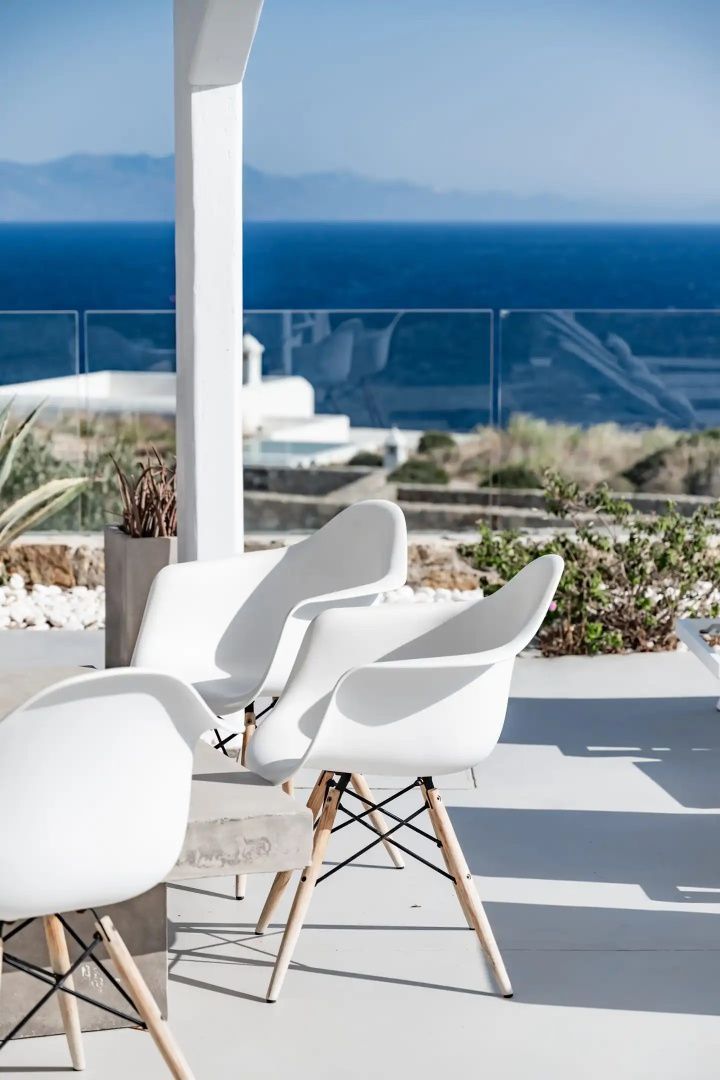 Moderne weiße Stühle stehen auf einer Terrasse mit Blick auf das Meer.