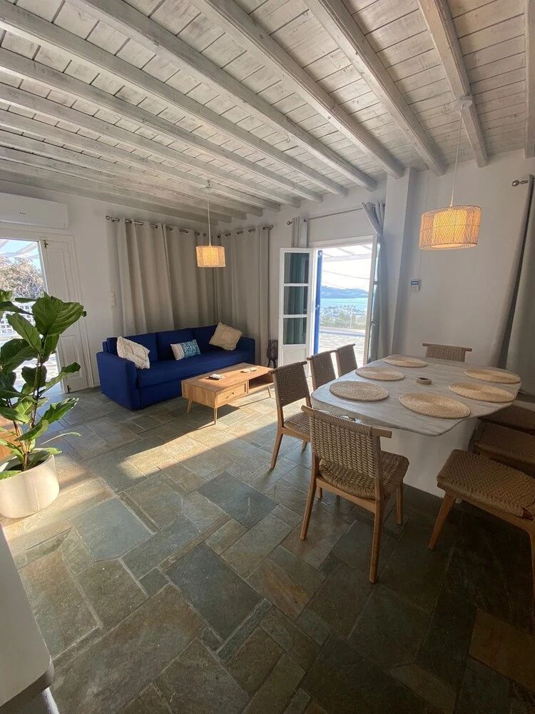 Wohnraum mit blauem Sofa, Esstisch und Blick durch die geöffnete Tür nach draußen.