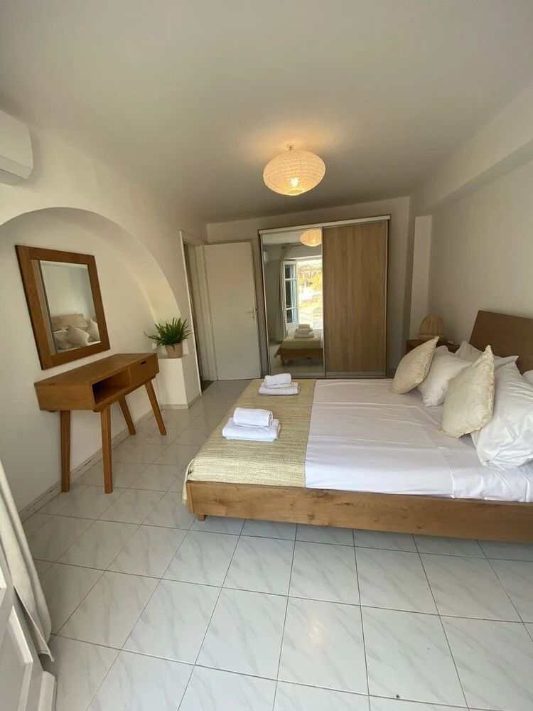 Hell eingerichtetes Schlafzimmer mit Doppelbett, Holzmöbeln und Fliesenboden.