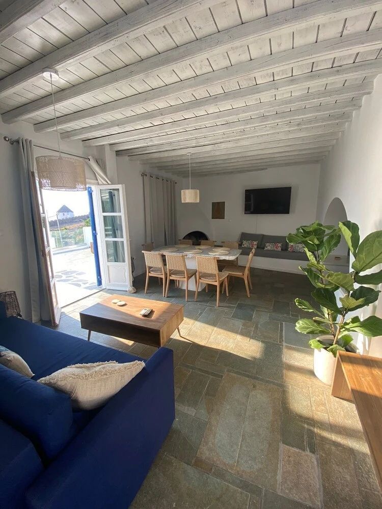 Wohnbereich mit blauem Sofa, Esstisch und Blick durch die geöffnete Tür auf die Terrasse.