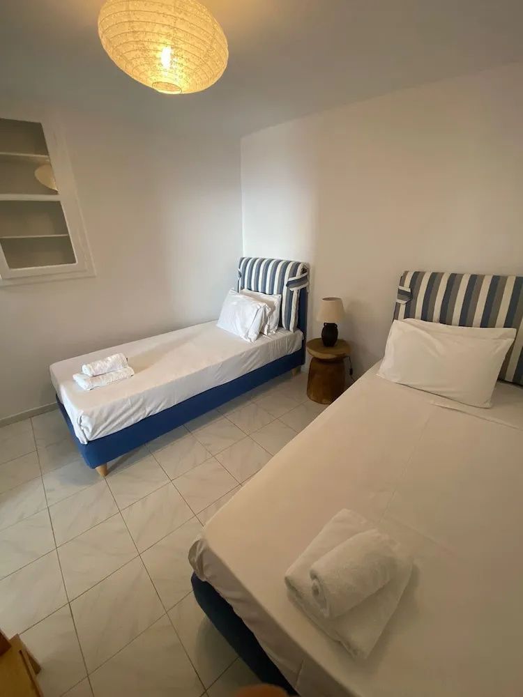 Schlafzimmer mit zwei Einzelbetten, blau weiß gestreiften Kopfteilen und hellem Fliesenboden.