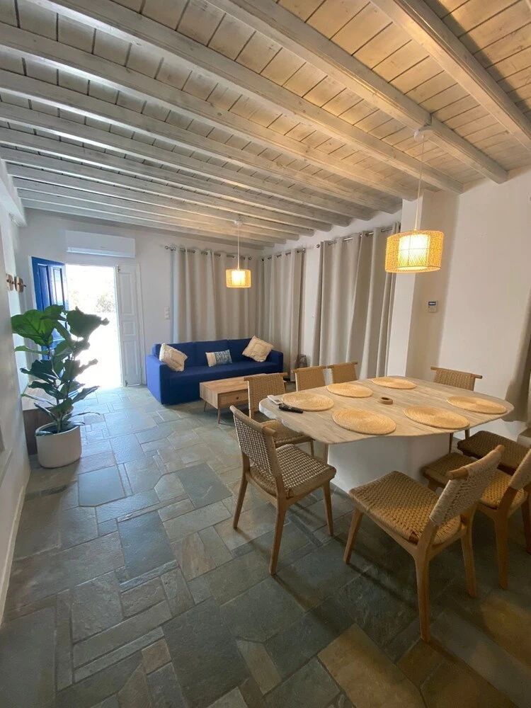 Essbereich mit hellem Esstisch, Stühlen, blauem Sofa und Holzbalkendecke.