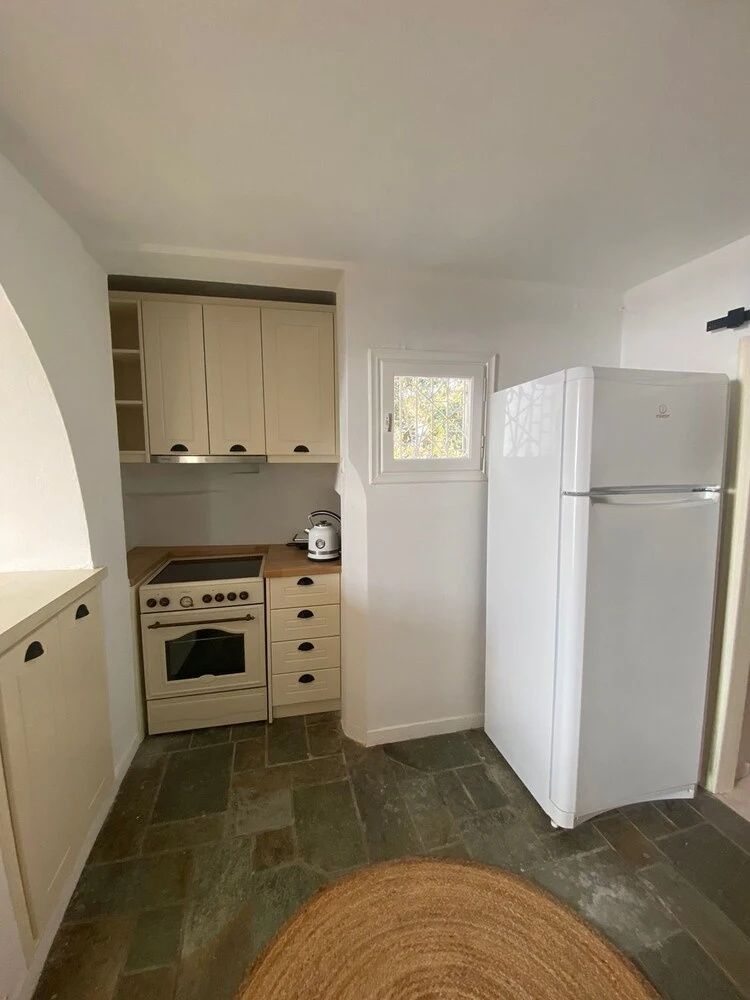 Kleine Küche in einer Unterkunft mit Herdkombination, weißem Kühlschrank und Steinboden.