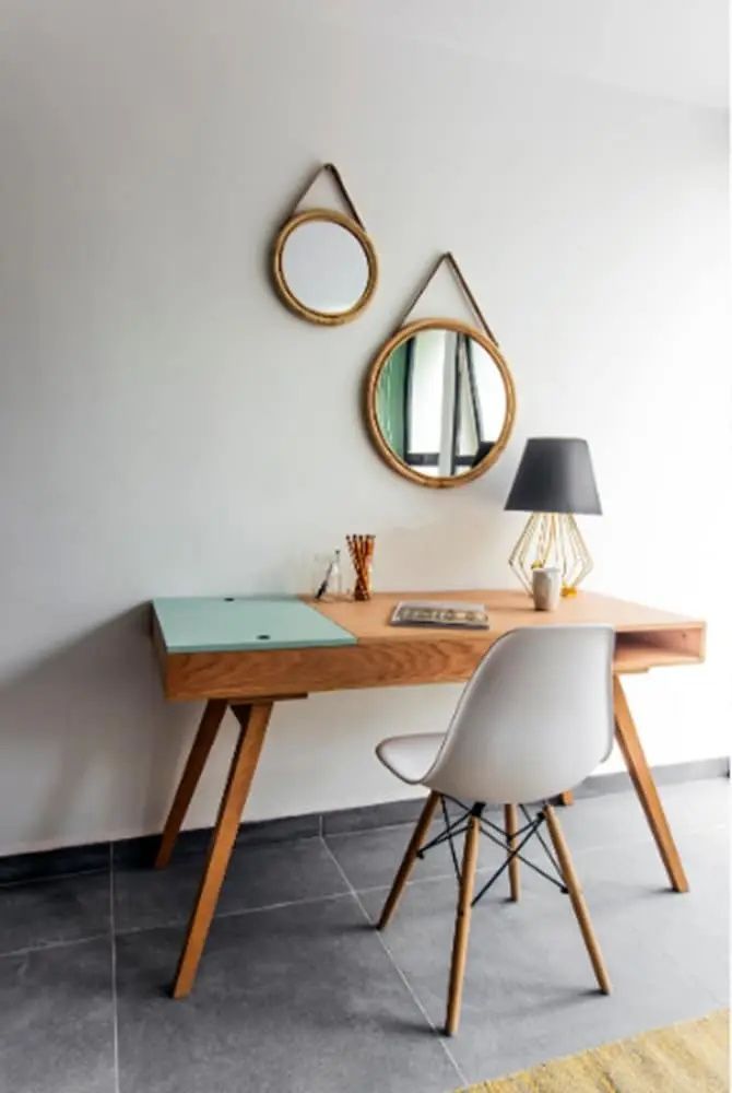 Holzschreibtisch mit Stuhl, Tischlampe und zwei runden Spiegeln an der Wand.