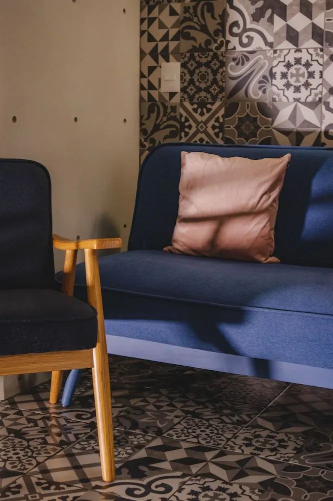 Blaues Sofa mit rosa Kissen und ein dunkler Sessel in einer Sitzecke.