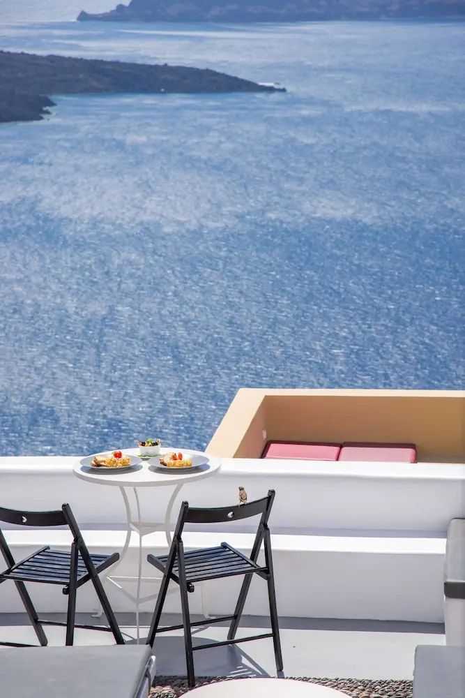 Tisch und zwei Stühle auf einer Terrasse mit freiem Blick auf das weite blaue Meer.