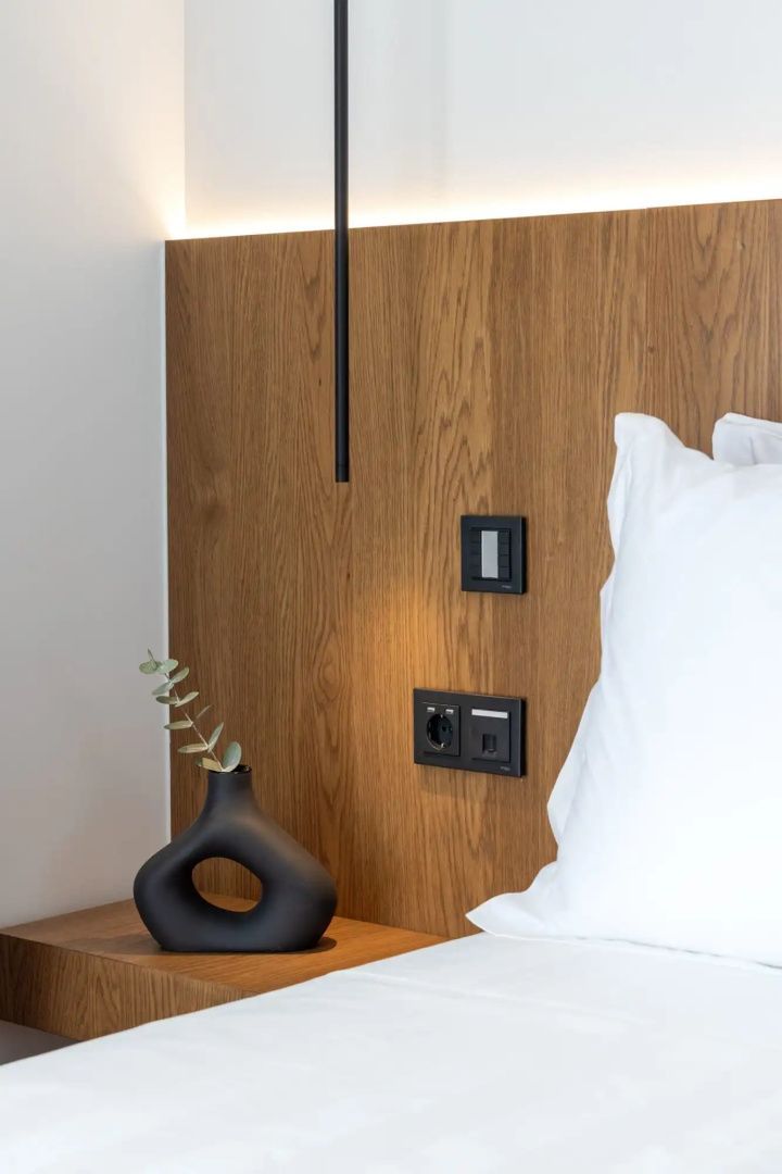 Nachttisch aus Holz mit schwarzer Vase, Eukalyptuszweig und Schaltern an der Wand.