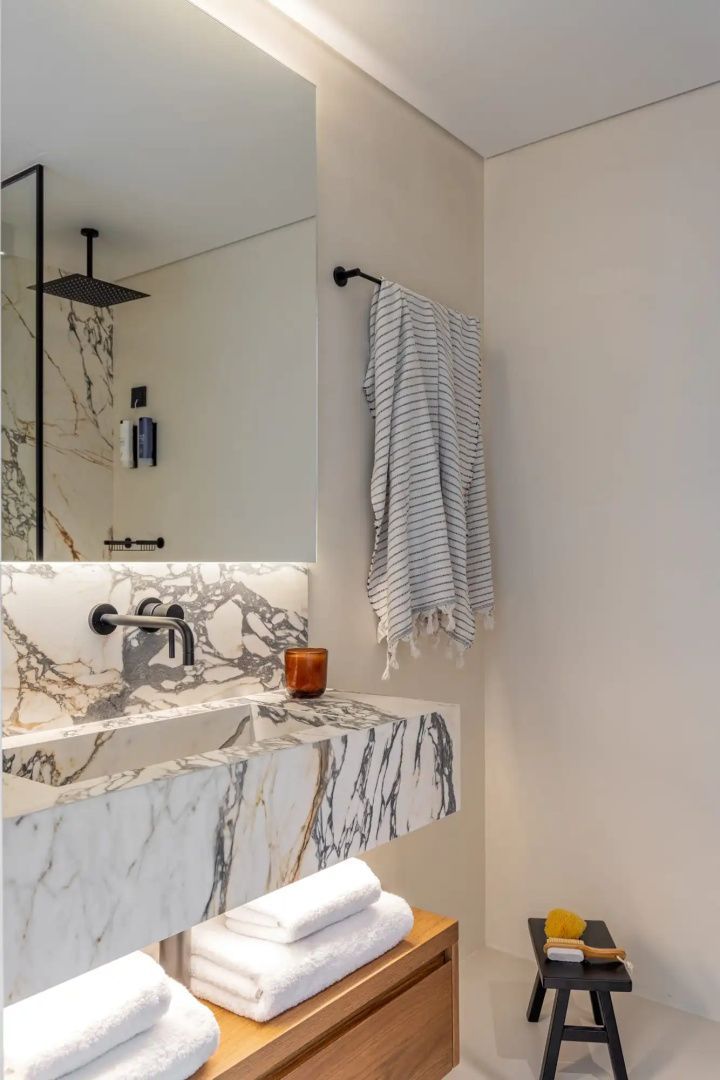 Modernes Badezimmer mit Marmorwaschtisch, großem Spiegel und Duschbereich.
