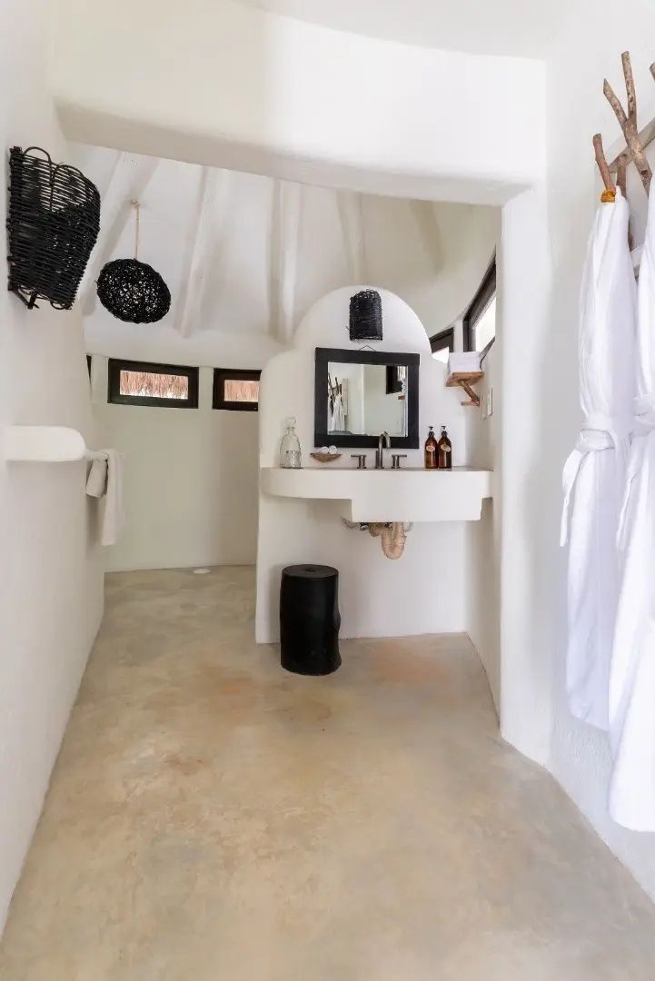 Weiß gestaltetes Badezimmer mit Waschtisch, Wandspiegel und aufgehängten Bademänteln.