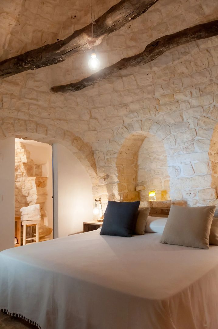 Schlafzimmer in einem Gewölbe aus Naturstein mit Doppelbett und Holzbalken.
