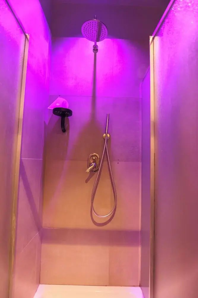 Duschkabine im Badezimmer mit violetter Beleuchtung und an der Wand montierter Brause.