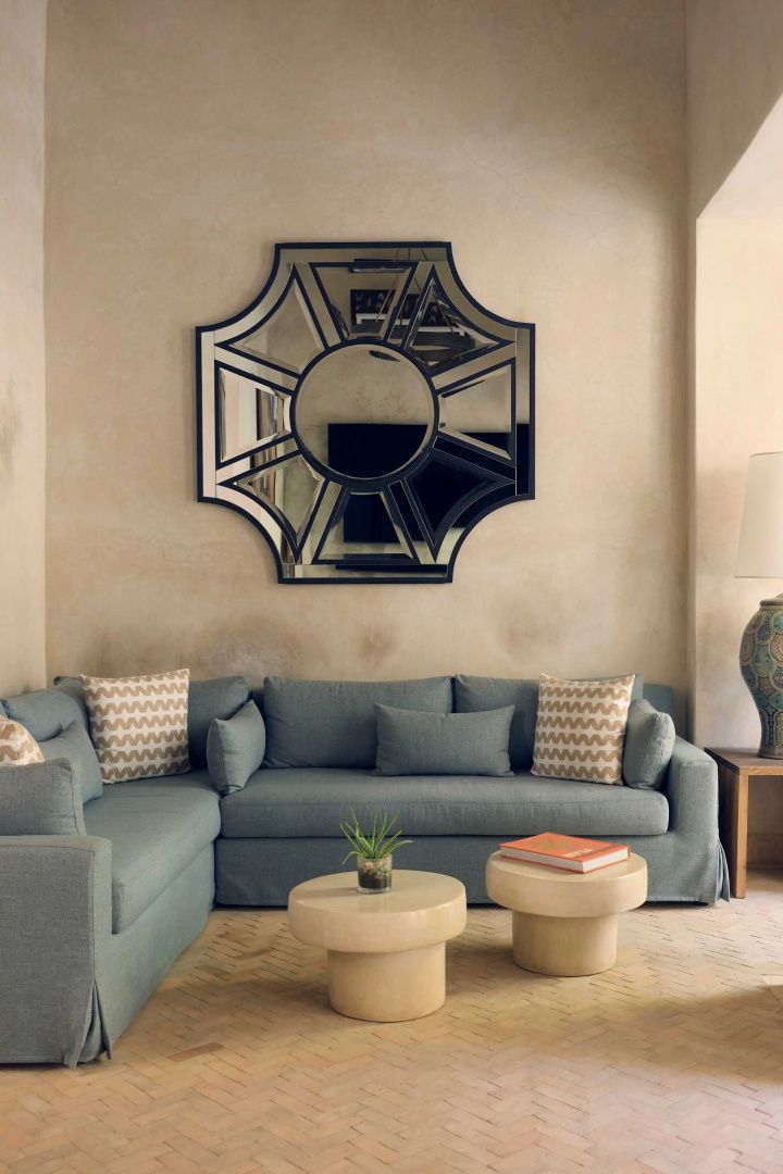 Sitzecke mit blauem Ecksofa, zwei kleinen Beistelltischen und einem geometrischen Wandspiegel.