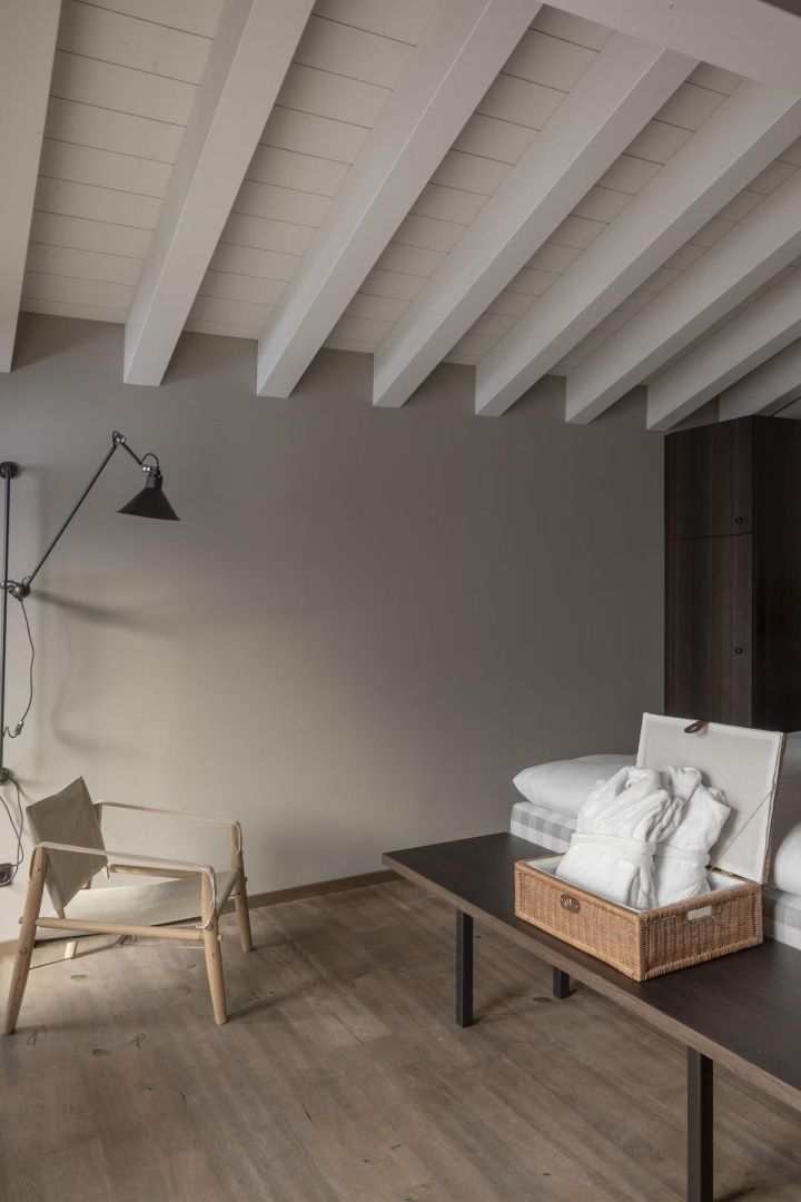 Helles Hotelzimmer mit Holzbalkendecke, einem Sessel und einem Korb mit Bademänteln.