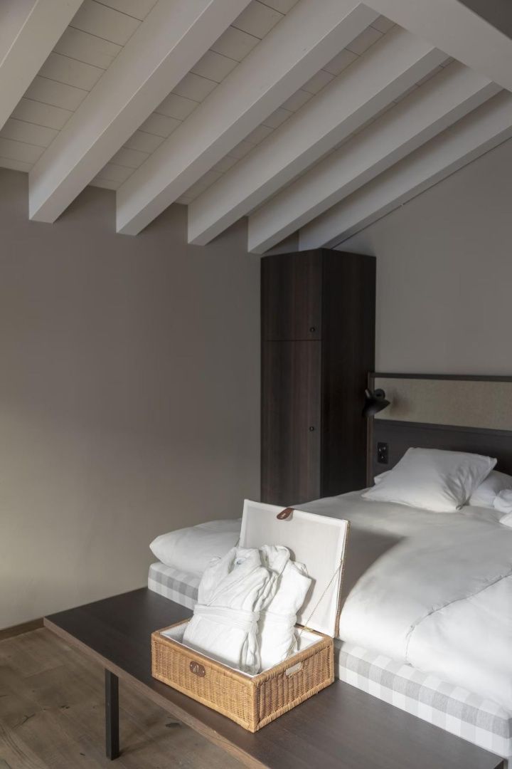 Doppelbett mit weißer Bettwäsche unter einer hellen Holzbalkendecke im Hotelzimmer.