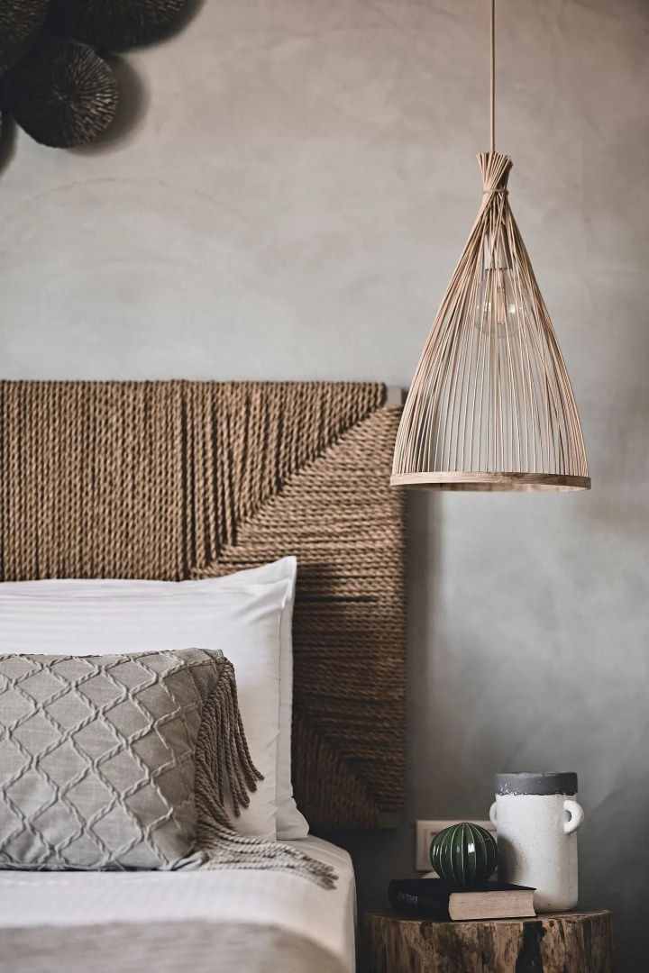 Bett mit strukturiertem Kissen, braunem Seilkopfteil und einer hängenden Holzleuchte.