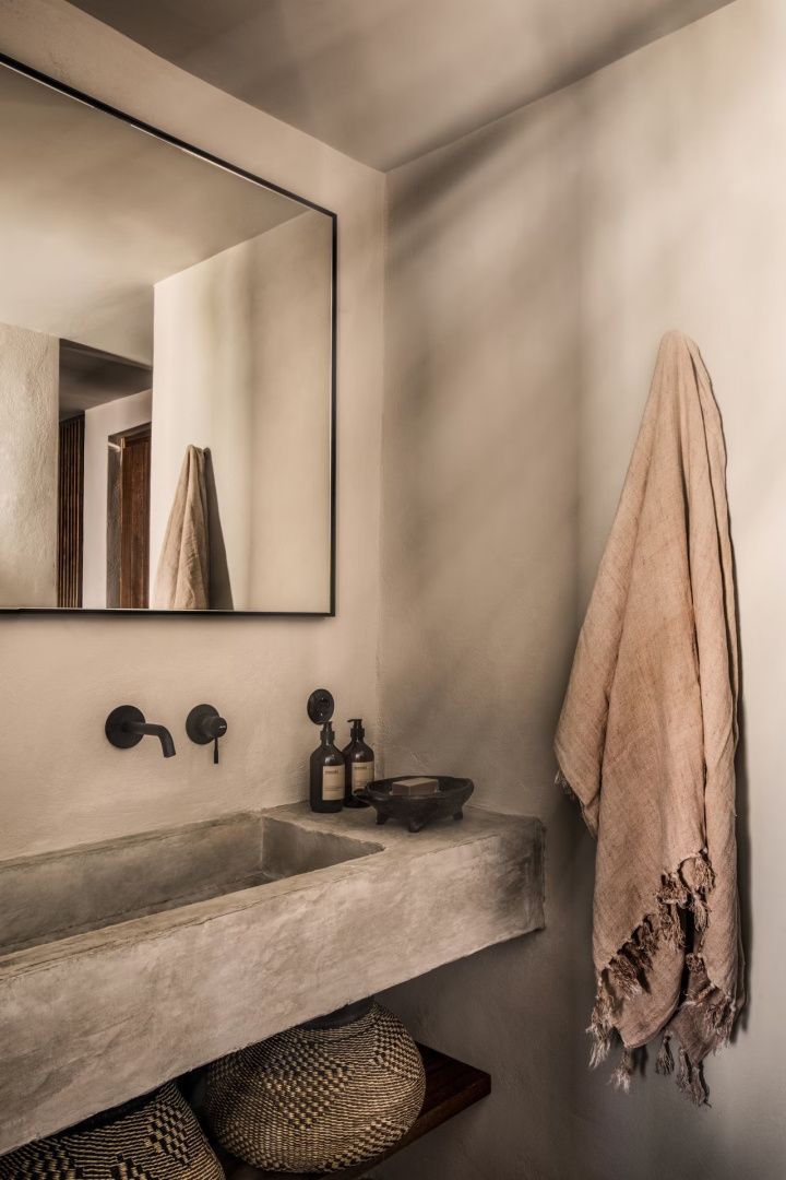 Waschtisch aus Beton mit schwarzer Armatur, Spiegel und Hängehandtuch im Badezimmer.