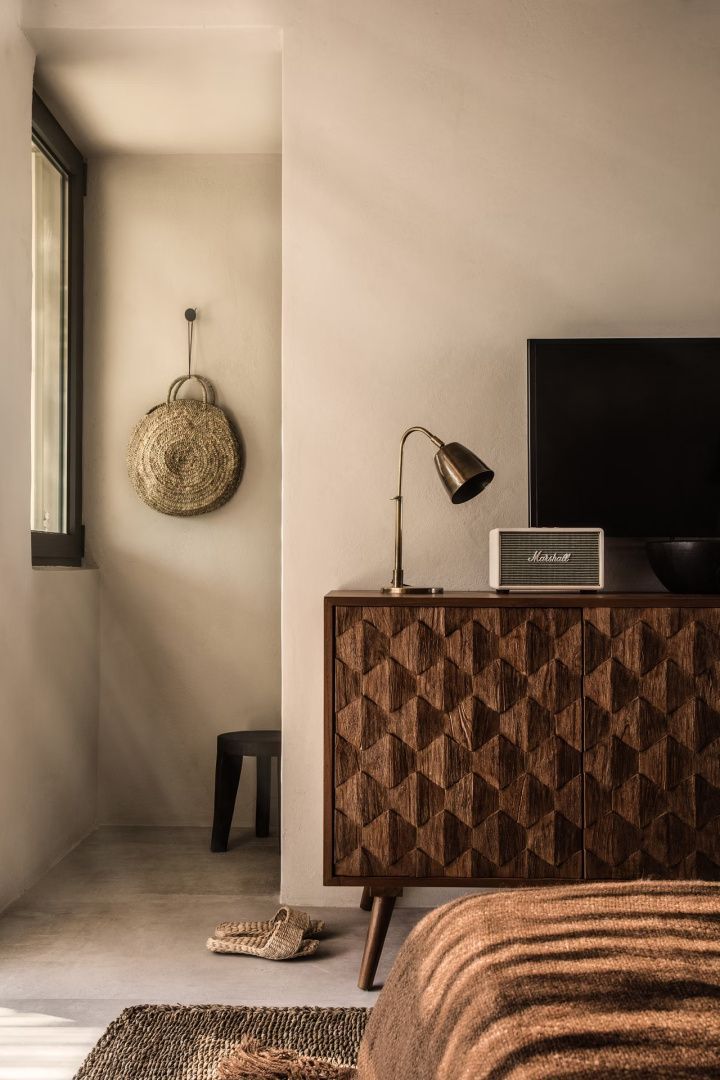 Holzkommode mit strukturierter Front, Retro-Tischleuchte, Lautsprecher und Tasche an der Wand.