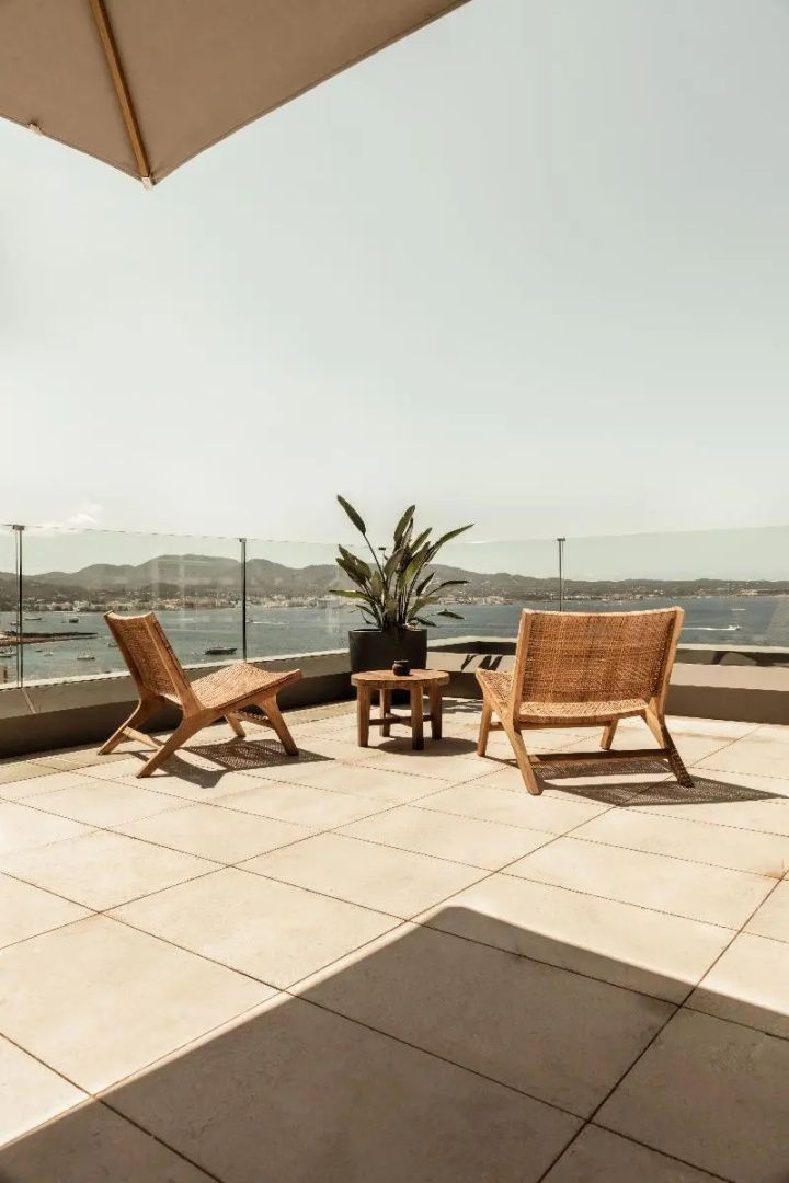 Sonnige Dachterrasse mit zwei Holzstühlen, einem kleinen Tisch und weitem Blick auf die Meeresbucht.