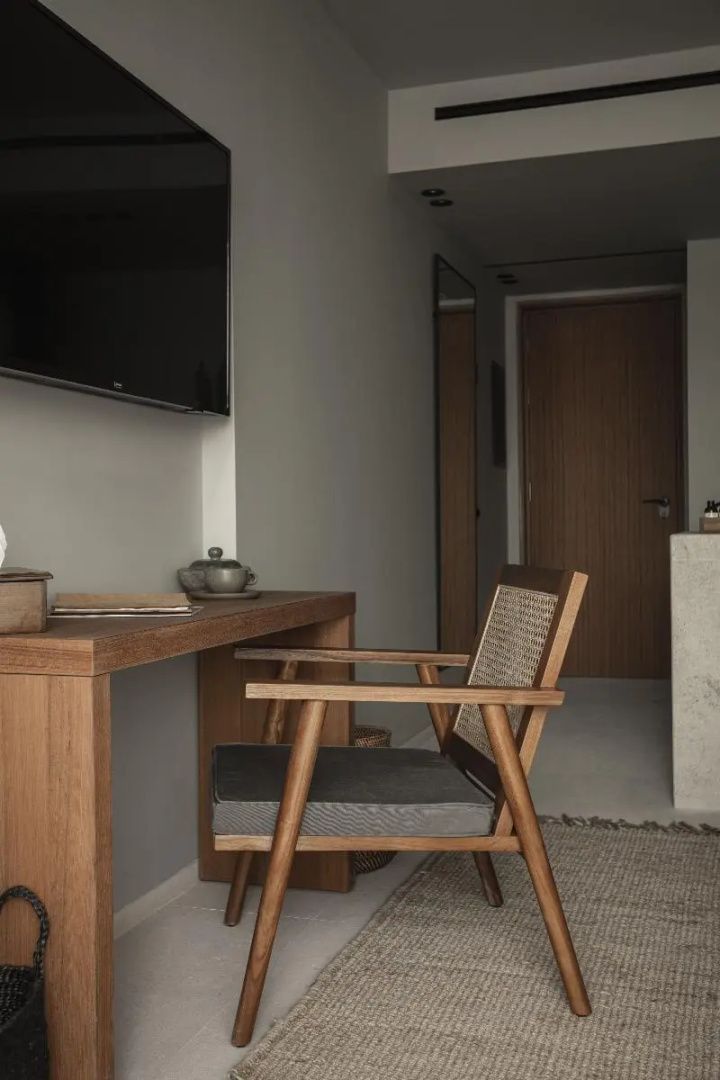 Schreibtisch aus Holz mit dazu passendem Stuhl aus Geflecht in einem Hotelzimmer.