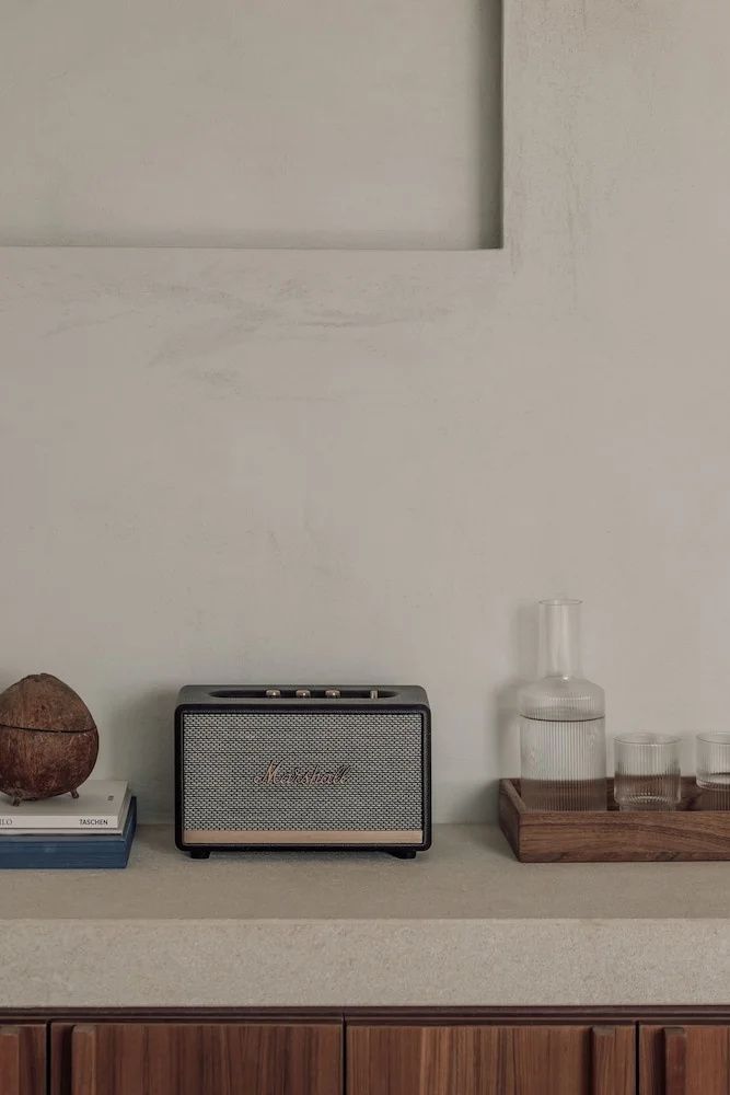 Bluetooth Lautsprecher, Glaskaraffe und Trinkgläser auf einer beigen Ablage im Zimmer.