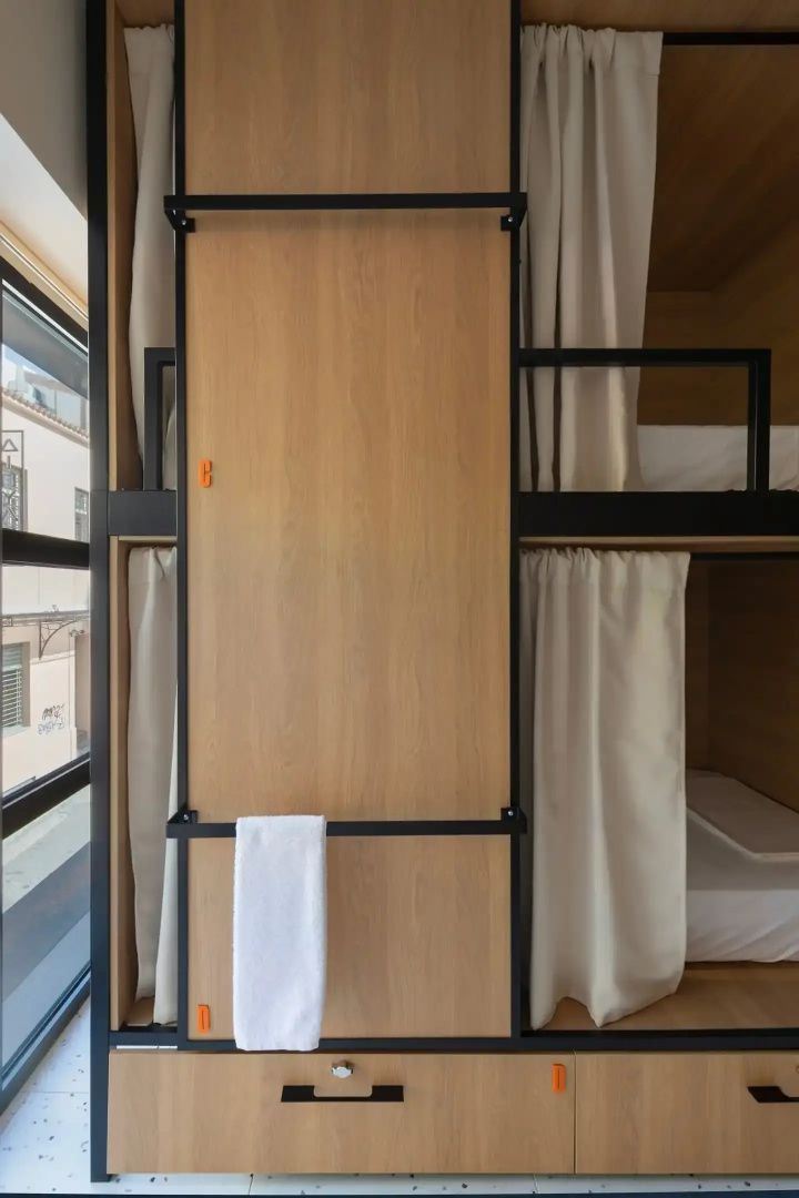 Holzbetten in einem Schlafsaal mit Vorhängen für Privatsphäre und Fenster zur Straße.
