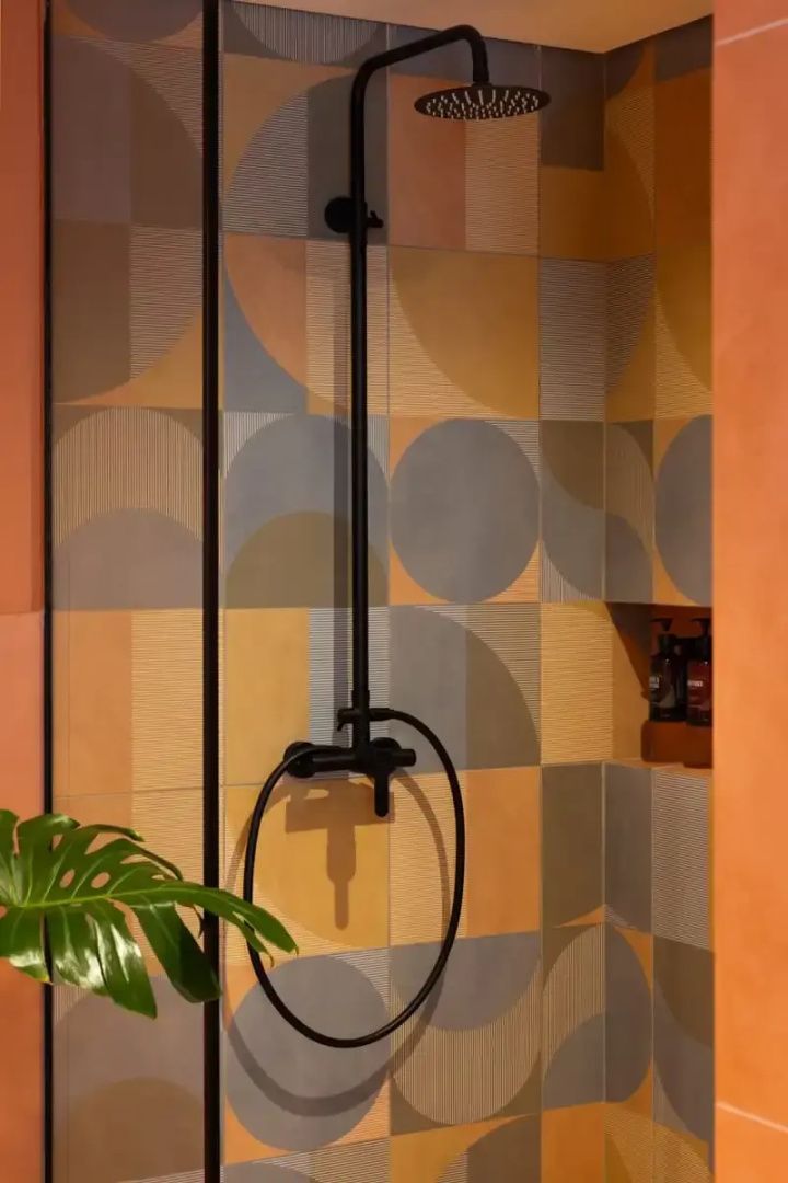 Moderne Dusche mit schwarzen Armaturen und geometrisch gemusterten Fliesen an der Wand.