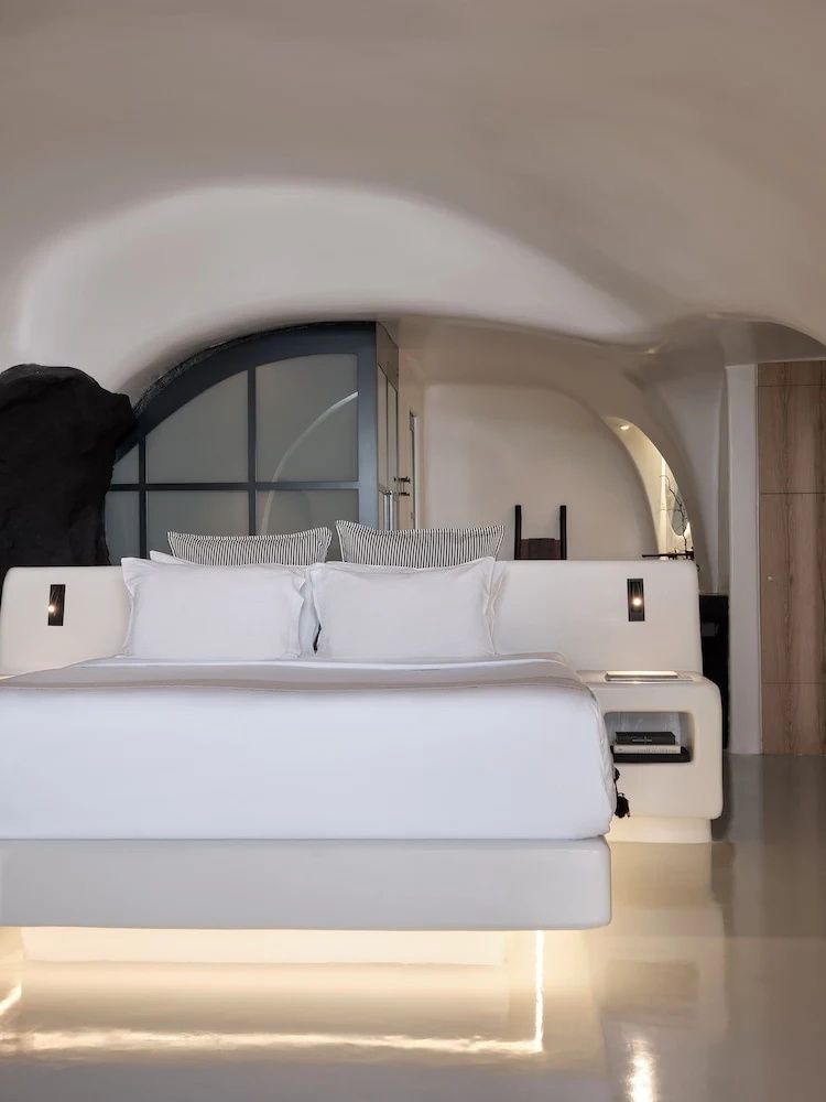 Doppelbett in einer weiß getünchten Höhlensuite mit geschwungenen Wänden und dezenter Beleuchtung.