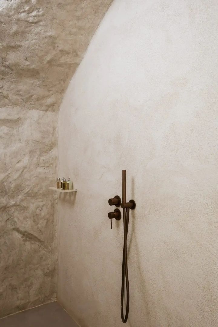 Eine Dusche mit dunkler Metallarmatur an einer rau strukturierten Wand.