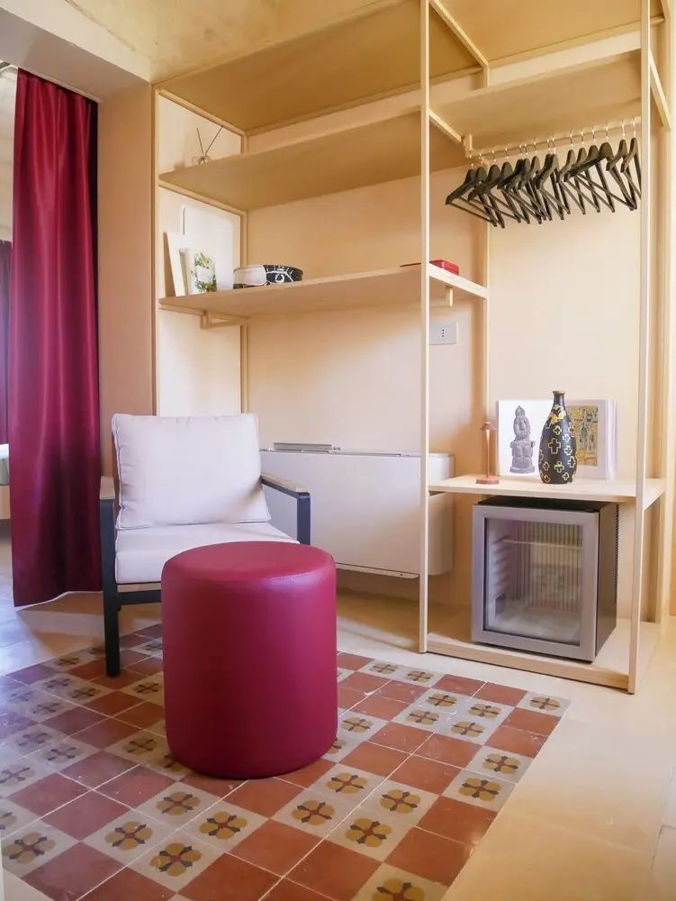 Offener Kleiderschrank aus Holz mit integrierter Minibar, Kleiderbügeln und einem Hocker.