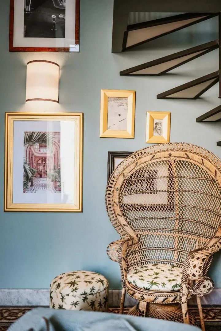 Sessel aus Geflecht vor einer blauen Wand mit eingerahmten Kunstdrucken.