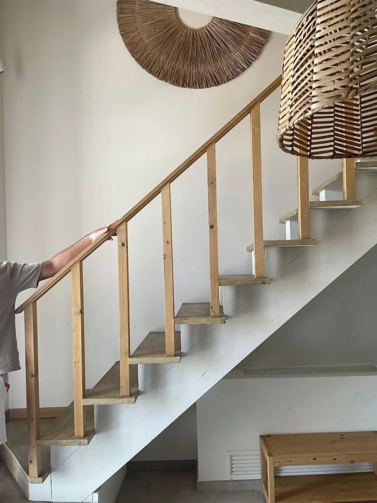 Holztreppe mit schlichtem Geländer führt in den oberen Bereich eines hellen Zimmers.