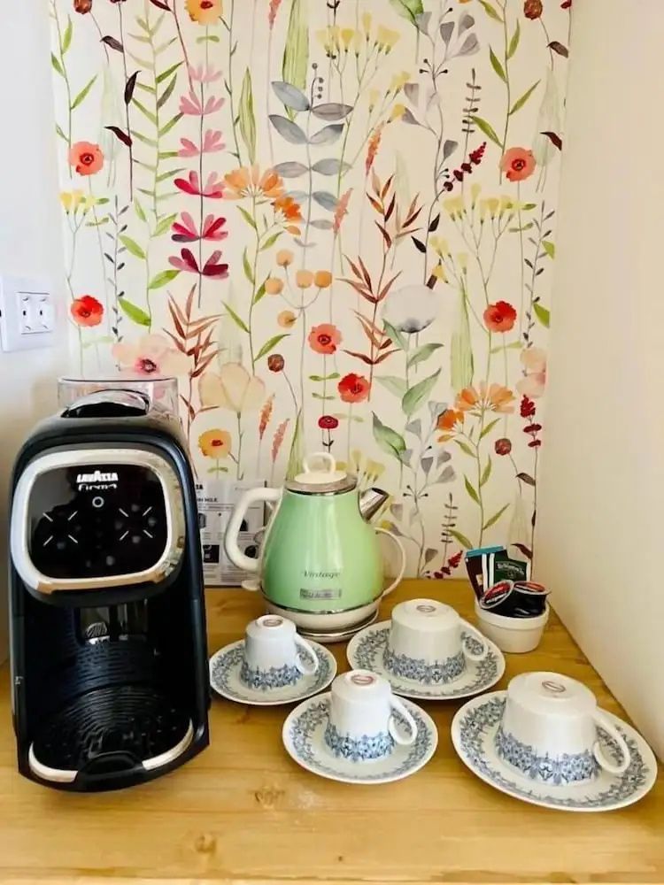 Kaffeemaschine, grüner Wasserkocher und Tassen stehen vor einer bunt bemalten Wand.