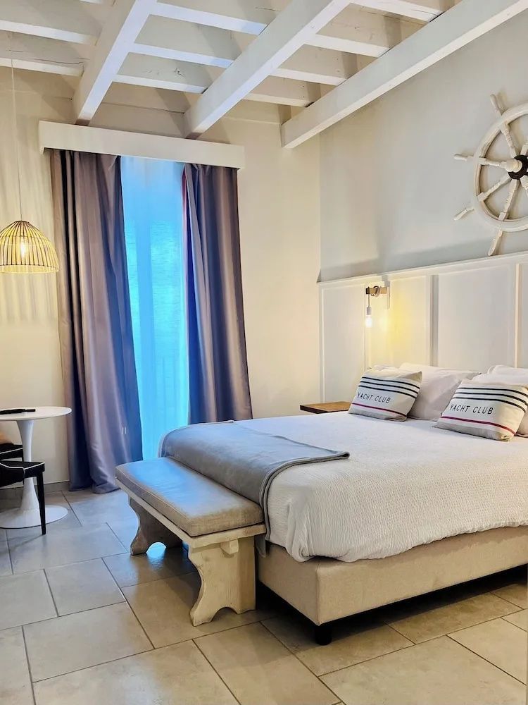 Hotelzimmer mit weißem Doppelbett, Holzbank und dekorativem Steuerrad an der Wand.