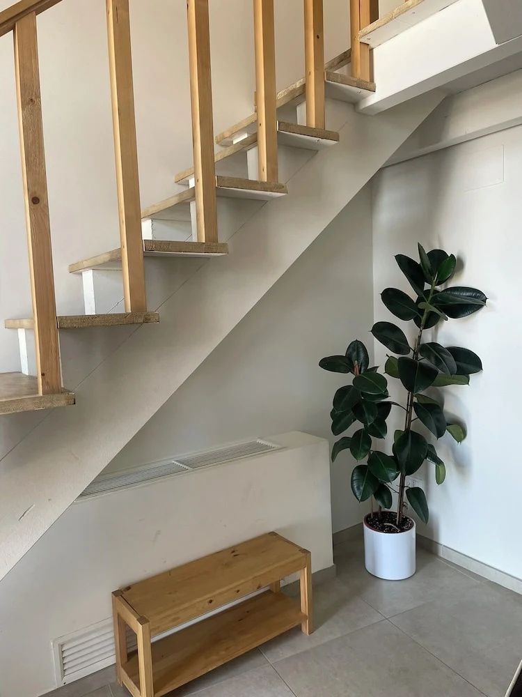 Unterseite einer Holztreppe mit Holzbänkchen und einer Zimmerpflanze im Topf.