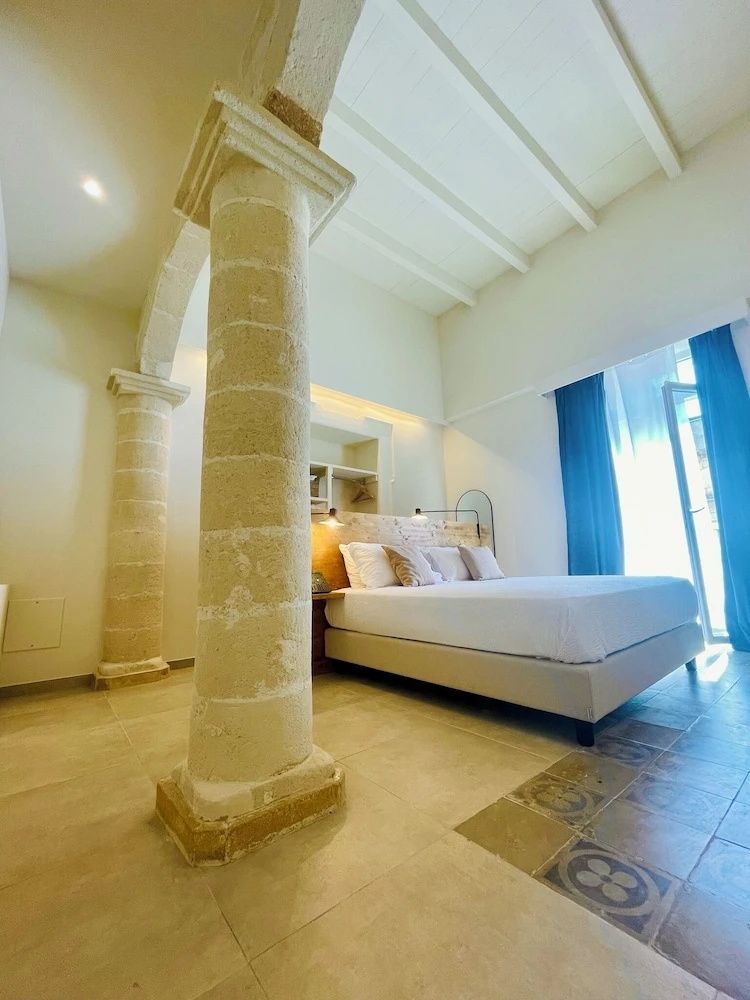 Hell eingerichtetes Hotelzimmer mit historischen Steinsäulen und Doppelbett.