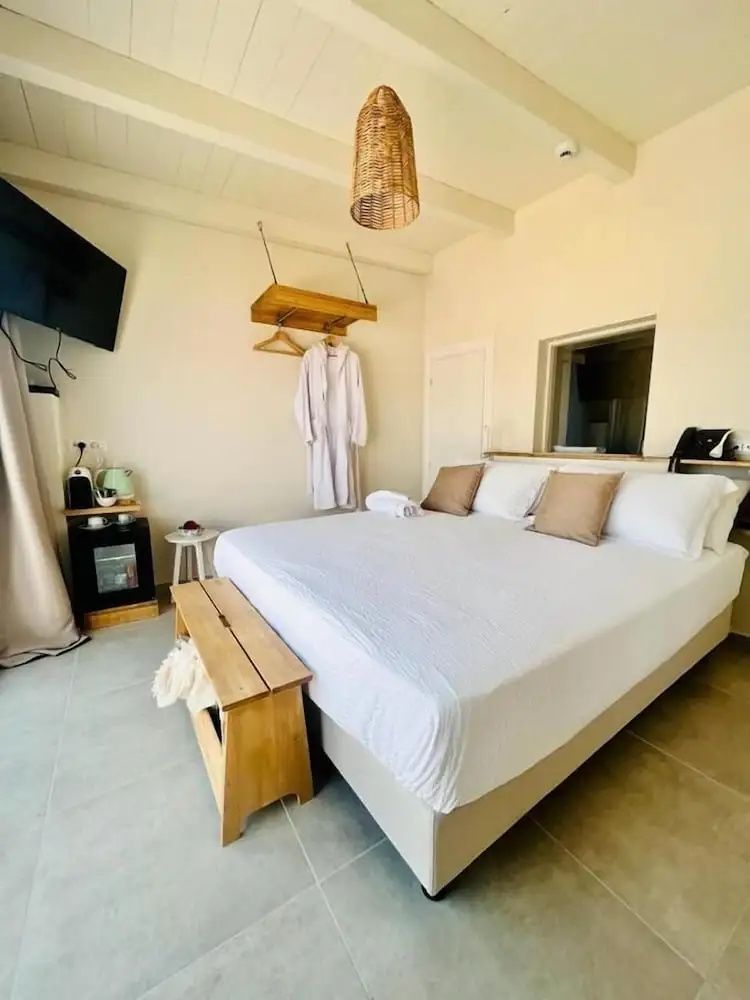 Helles Schlafzimmer mit großem Bett, Holzbank, Bademantel und Mini-Kühlschrank.