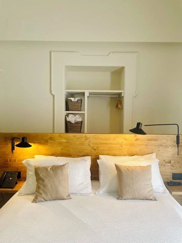 Doppelbett mit weißer Bettwäsche, Holzkopfteil, Wandleuchten und eingebauter Wandnische.