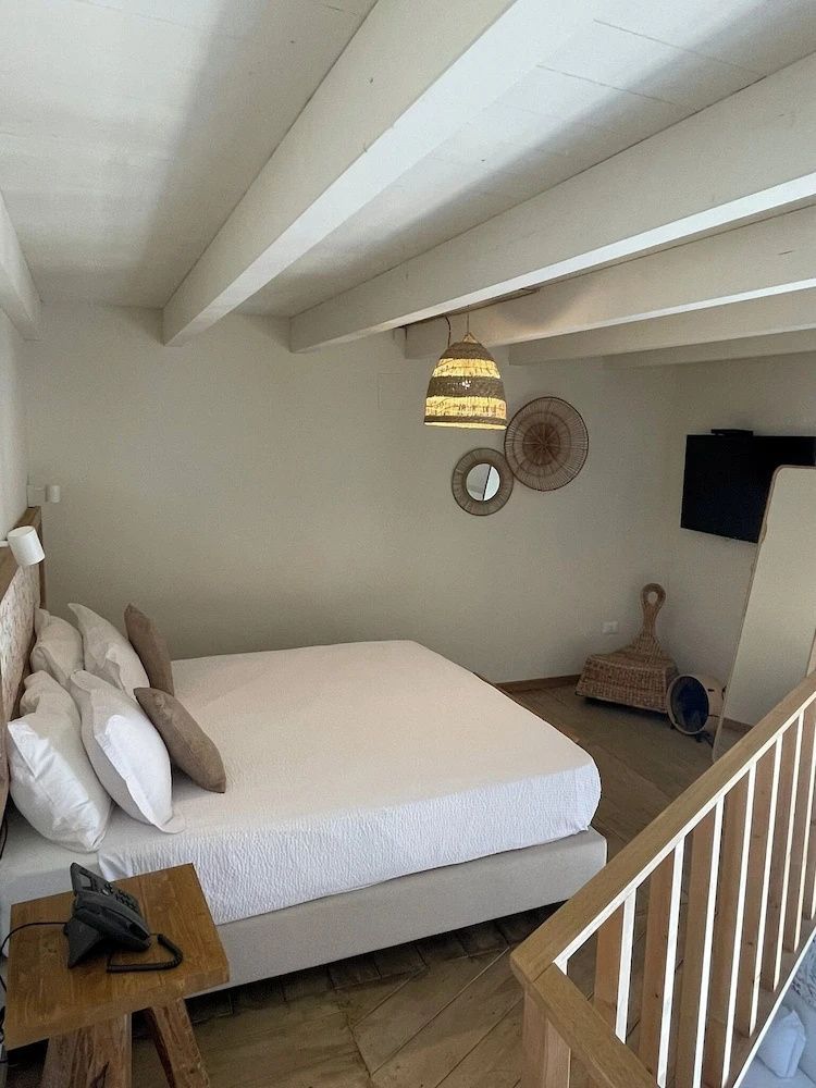 Doppelbett mit weißer Bettwäsche unter einer hellen Holzbalkendecke im Hotelzimmer