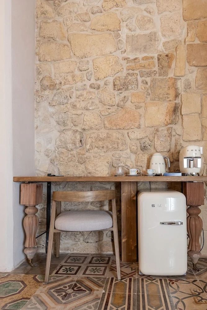 Schreibtisch aus Holz an einer Natursteinwand mit Minikühlschrank und Wasserkocher.