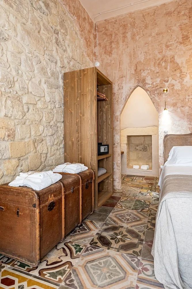 Schlafzimmer mit historischem Fliesenboden, offenem Holzschrank und Steinwänden.