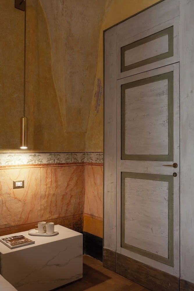 Ecke eines Hotelzimmers mit bemalten historischen Wänden, Hängelampe und weißem Nachttisch