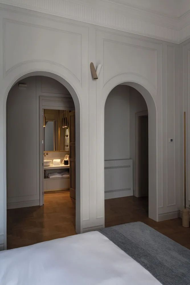Zwei Rundbögen in einer hellen Wand geben den Blick auf ein beleuchtetes Badezimmer frei.