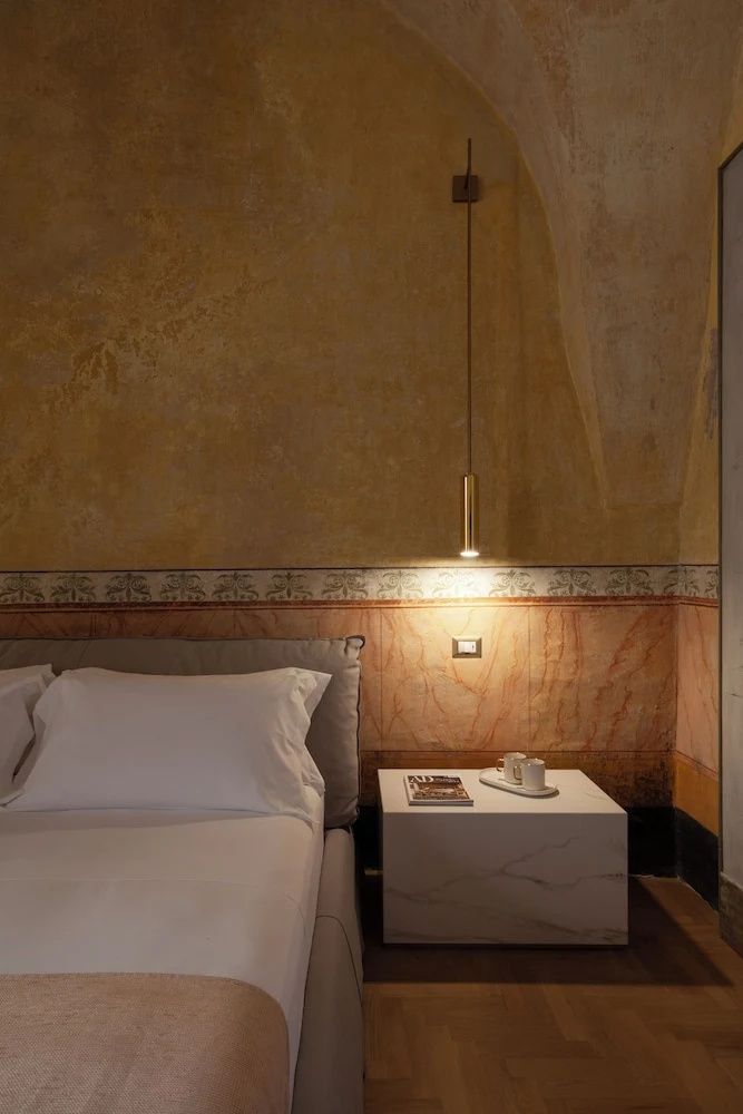 Hotelzimmer mit weißem Doppelbett, modernem Nachttisch und bemalter historischer Wand