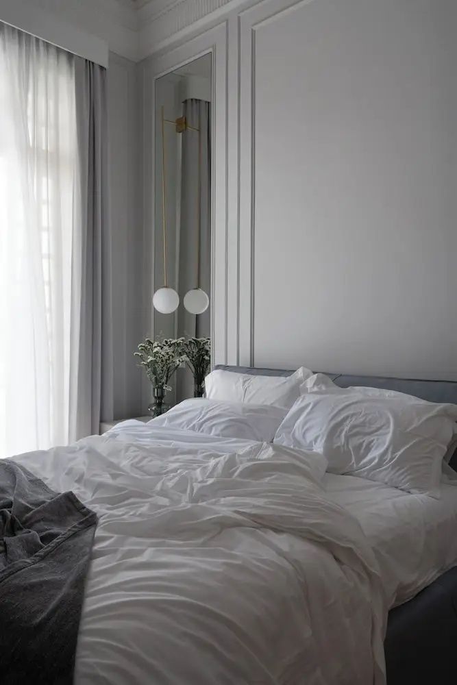 Doppelbett mit weißer Bettwäsche neben einem Fenster und hängenden Kugellampen.